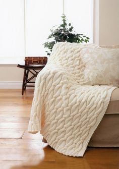 a white blanket sitting on top of a couch next to a potted green plant