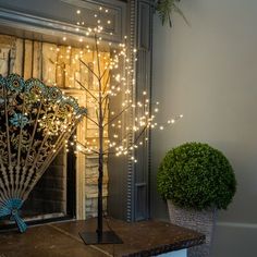 a decorative tree with lights on it next to a potted plant and window sill