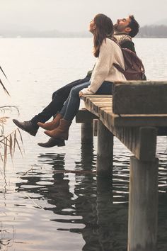 two people are sitting on a dock and one is kissing the other's forehead