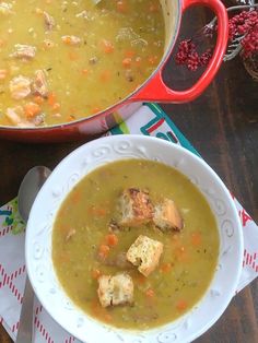 there is a bowl of soup with croutons in it and a red pot next to it