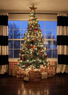 a decorated christmas tree in front of a window with black and white striped drapes