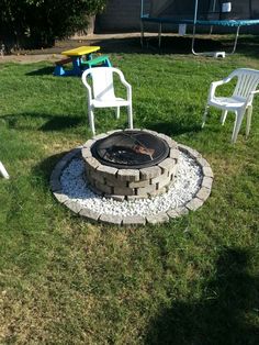 a fire pit sitting in the middle of a lawn next to two chairs and a table