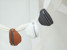 three purses hanging from the side of a white curtain with zippers on them