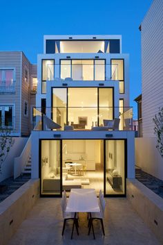 a table and chairs in front of a modern house at dusk with stairs leading up to the upper level