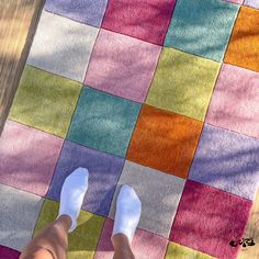 a person standing on top of a wooden floor next to a multi colored blanket and white shoes