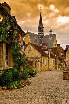 an old cobblestone street with buildings and a church steeple in the background