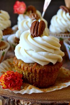 cupcakes with white frosting and pecans are on a wooden tray, ready to be eaten