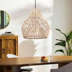 a dining room table with chairs and a light hanging from the ceiling over it, next to a potted plant