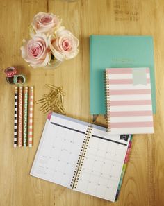 a wooden table topped with pink roses and notebooks next to scissors, pencils and markers