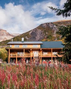 a large wooden house sitting on top of a lush green hillside next to tall grass