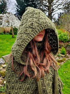 a woman wearing a green knitted hooded jacket and matching hat with her hair in the wind