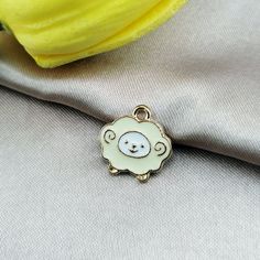 a white sheep charm sitting on top of a piece of cloth next to a yellow flower