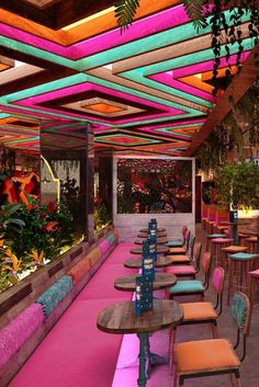 the inside of a restaurant with tables and chairs covered in bright colored cloths, plants and flowers