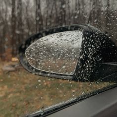 the rear view mirror of a car with rain drops on it and trees in the background