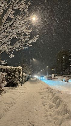 a snow covered street at night with cars parked on the side