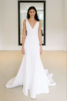 a woman in a white wedding dress standing in front of a mirror with her hands on her hips