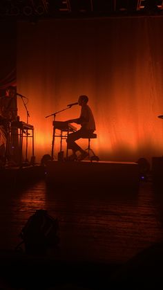 two people sitting on stools in front of a stage with an orange light behind them