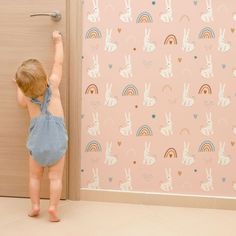 a toddler reaching up to the wall in front of a door with rabbits and rainbows on it