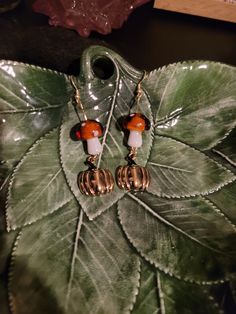 a pair of earrings sitting on top of a green leaf next to a red and white bead