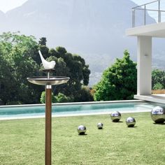 some silver balls are in the grass near a pool and mountain side house with mountains in the background