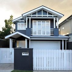 a white picket fence in front of a blue and gray house with two story windows