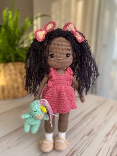 a crocheted doll holding a stuffed toy elephant on a wooden table next to a potted plant