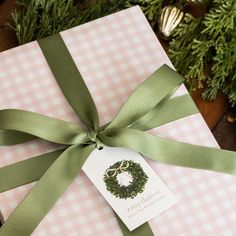 a present wrapped in pink and green ribbon with a wreath on it's tag