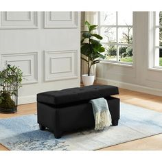 a black ottoman sitting on top of a rug in front of a white wall and windows