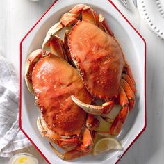 two large crabs on a plate with lemon wedges and sauce next to it, ready to be eaten