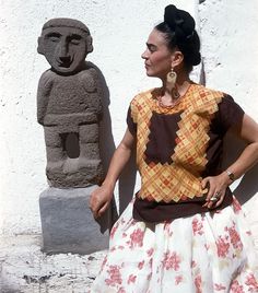 a woman standing in front of a stone statue and wearing a dress with flowers on it