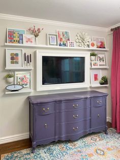 a living room with a large tv mounted on the wall and purple dressers in front of it