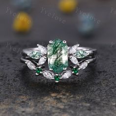 a green and white ring sitting on top of a black stone surface with leaves around it