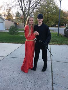 a man and woman dressed up in costume posing for a photo on the sidewalk with swords