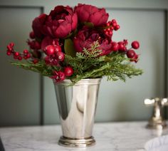 a silver vase filled with red flowers and greenery