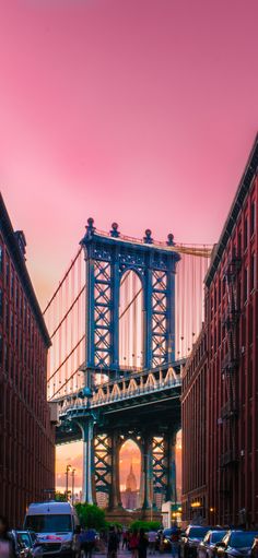 people walking on the sidewalk in front of tall buildings with a bridge over them at sunset