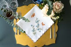 a place setting with flowers and silverware on a yellow plate, next to wine glasses