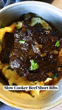 a close up of a bowl of food with meat and potatoes in it on a table