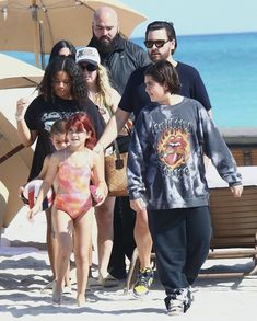 a group of people walking on the beach with one woman in a bathing suit and another man in a baseball cap