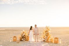 a bride and groom standing in front of an altar with flowers on the beach at sunset