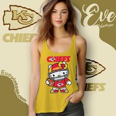 Kansas City Chiefs Hello Kitty Shirt The Kansas City Chiefs Hello Kitty Shirt is an adorable fusion of football and fun. This design showcases Hello Kitty dressed up in the Chiefs’ iconic red and yellow football gear, complete with a helmet and jersey featuring the team’s logo. It’s a perfect way to celebrate your love... Fan Apparel Tops With Character Print For Sports Events, Sports Fan Apparel Tops With Character Print, Sporty Tops With Character Print For Sports Events, Game Day Yellow Graphic Print Tops, Yellow Graphic Print Top For Game Day, Yellow Tops For Sports Events, Yellow Sports Tops With Team Name, Sporty Yellow Top Fan Merchandise, Hello Kitty Shirt