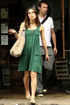 a woman in a green dress is walking past a man with a bag on his shoulder