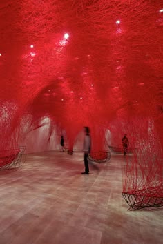 people are walking through an art installation with red lights on the ceiling and wooden floors