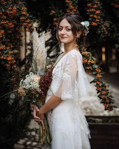 a woman in a white dress holding a bouquet of flowers and greenery on her wedding day