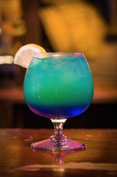 a blue and green drink sitting on top of a table next to a slice of lemon