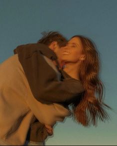 a man and woman kissing each other in front of a blue sky with the sun behind them