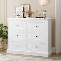 a white dresser sitting in a room next to a potted plant and framed pictures