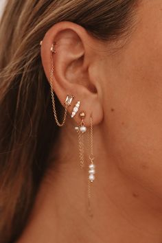 a close up of a person wearing gold ear chains and pearl drop earrings with pearls on them