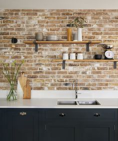 a kitchen with brick wall and wooden shelves above the sink, surrounded by white counter tops