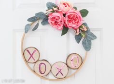 a wreath made out of wood slices with pink flowers on top and the word xo spelled