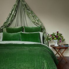 a bed with green bedspread and pillows in a room next to a table